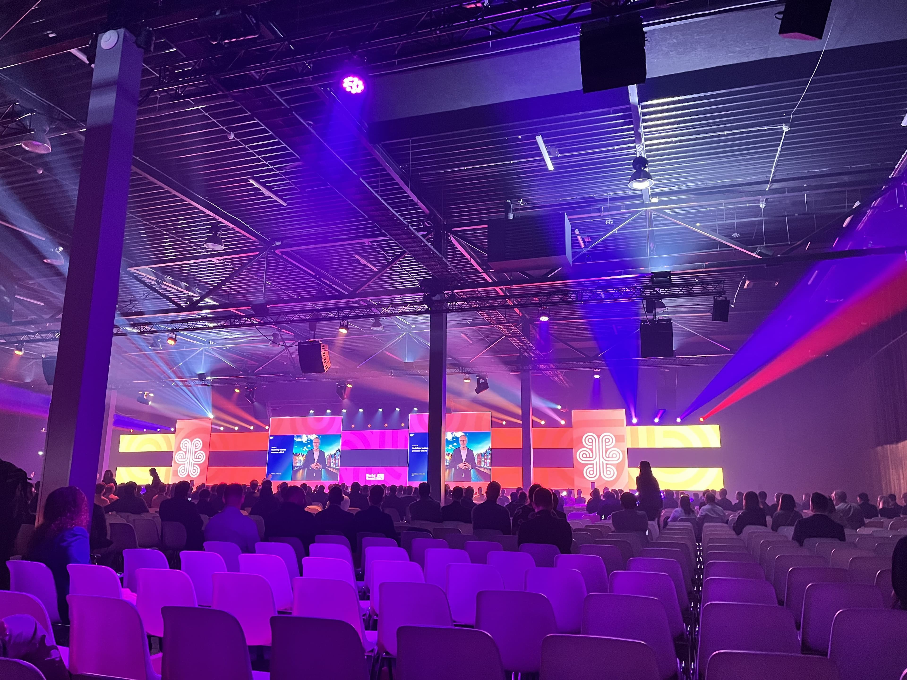 Auditorium des World Summit AI mit bunter Bühnenbeleuchtung. -- Bühne des World Summit AI in stimmungsvoller Beleuchtung und voller Zuschauer.